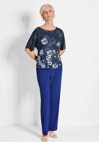 Marineblauw bloemen top met korte mouwen, met witte en blauwe rozenpatronen. Gecombineerd met koningsblauwe broek en lichte sandalen.