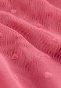 Rosa nätmaterial med små upphöjda hjärtformade mönster och mjuka veck som skapar textur och djup.