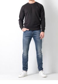 Svart crewneck sweatshirt, denim jeans och vita sneakers. Tygerna har en slät yta. Jeansen har en blekt blå tvätt med lätt slitningar.