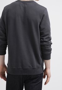 Felpa grigia a girocollo con polsini e orlo a coste, caratterizzata da una morbida texture e una vestibilità rilassata. Nessun logo o motivo visibile.