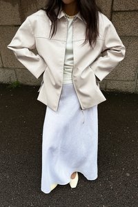 Šviesiai smėlinė odinė striukė, balta prigludusi palaidinė, tekstūruotos baltos maksi sijonas ir šviesiai geltoni aukštakulniai. Striukė turi užtrauktuką ir laisvą siluetą.