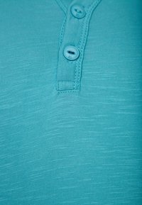 Tyrkysová košile s krátkým rukávem z texturované látky, s třemi plastovými knoflíky na výstřihu a jemnými vodorovnými pruhy.