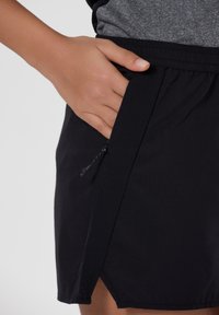 Shorts de sport noirs avec une taille élastique et une poche latérale zippée. Fabriqués dans un tissu respirant avec de légères perforations pour la ventilation.