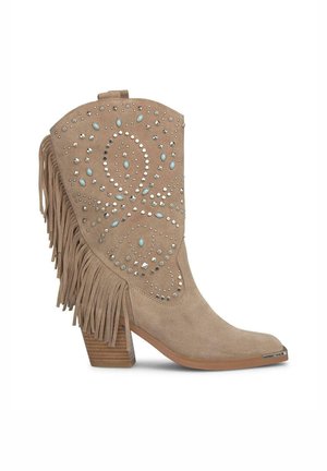 Botín de ante beige hasta el tobillo con flecos, tachuelas decorativas y un tacón bajo y apilado. Presenta una punta afilada y adornos detallados en el caño.