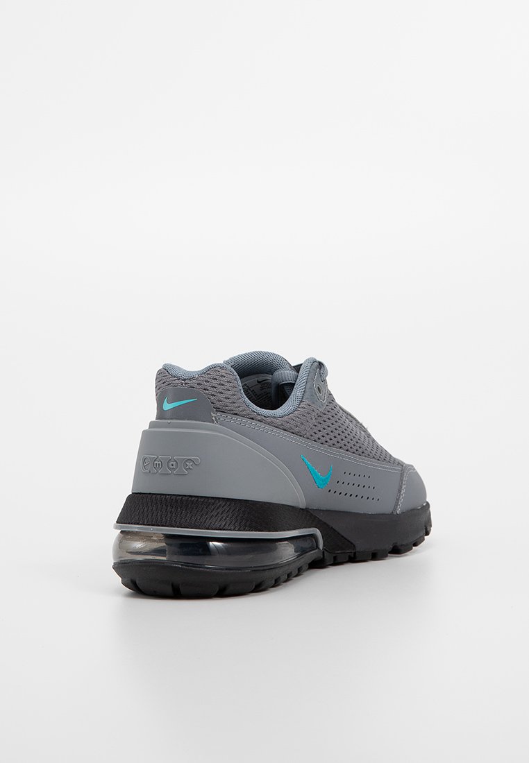 Zapatillas Nike grises con parte superior de malla, acentos turquesa y una media suela negra. Presenta una unidad de amortiguación de aire visible en el talón.