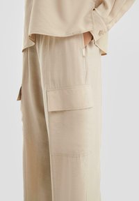 Beige, lichtgewicht, gestructureerde cargobroek met een relaxte pasvorm, voorzien van zijzakken en subtiele stiksels.