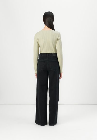 Olive green ribbed long-sleeve top paired with high-waisted black wide-leg jeans, featuring large back pockets and a straight cut.