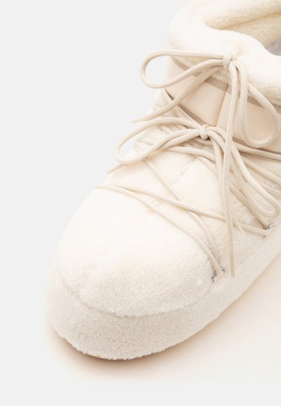 Botte d'hiver couleur crème avec un matériau épais et doux en polaire, des lacets en corde noués en nœuds et un col de cheville rembourré.