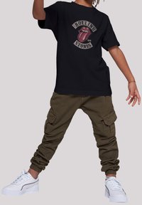 Sort bomulds T-shirt med Rolling Stones logo, parret med olivengrønne cargo bukser med sidelommer og elastiske manchetter, samt hvide sneakers.