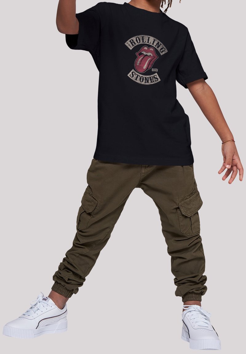 Sort bomulds T-shirt med Rolling Stones logo, parret med olivengrønne cargo bukser med sidelommer og elastiske manchetter, samt hvide sneakers.