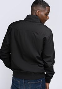 Chaqueta bomber negra con cuello alzado, puños de canalé y dobladillo elástico. Textura suave, diseño minimalista y sin patrones visibles.
