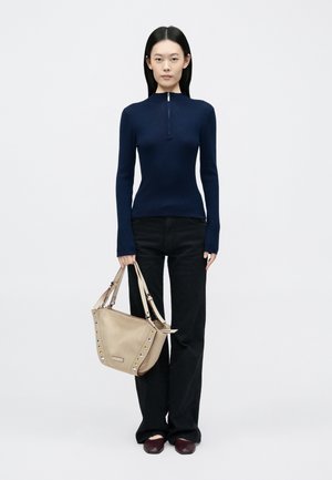 Μπλε σκούρο ριμπ μακρυμάνικο τοπ με φερμουάρ στον γιακά, μαύρο παντελόνι με καμπάνα, κρατώντας μια μπεζ τσάντα με καρφιά και ροζ λεπτομέρεια, σε συνδυασμό με μπορντό παπούτσια.