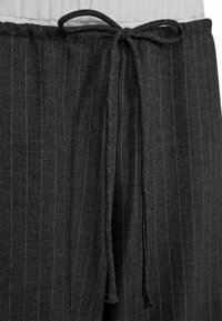 Black pinstripe trousers made of textured fabric, featuring a front tie closure. Stripes are subtle with hints of white thread.