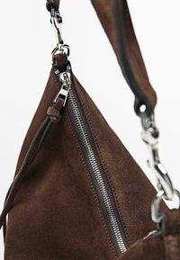 Hnědá semišová kabelka s stříbrným zipem, koženým popruhem a kovovými doplňky. Hladká textura s minimalistickým designem.