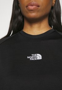 Juodas trumpas rankovės marškinėlis, pagamintas iš lygaus audinio, su baltu išsiuvinėtu "The North Face" logotipu kairėje krūtinės pusėje.