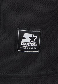 Crni materijal s teksturiranim uzorkom, na kojem se nalazi bijela pravokutna oznaka s "STARTER" logotipom i tekstom "BLACK LABEL" ispisanim podebljanim fontom.