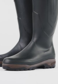 Čierne gumové čižmy s textúrovaným povrchom, pevná hnedá podrážka, drsný vzor dezénu a zosilnený zvršok pre odolnosť.