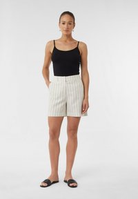 Schwarzes Tanktop kombiniert mit cremefarbenen Shorts mit vertikalen schwarzen Streifen, seitlichen Taschen und einer lässigen Passform. Schwarze Slide-Sandalen runden den Look ab.