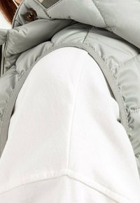 Grijze, donzige bodywarmer met een geribbelde kraag, gecombineerd met een wit shirt met lange mouwen met een gestructureerde afwerking en gestikte naaddetails.