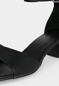 Μαύρο πέδιλο με ανοικτά δάχτυλα, λουράκι στον αστράγαλο και χαμηλό τετράγωνο τακούνι, λεία δερμάτινη επιφάνεια και ρυθμιζόμενο ασημένιο αγκράφα.