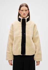 Φλις ζακέτα σε κρέμα με μαύρο μπροστινό πάνελ, διαθέτει υψηλό γιακά, κουμπιά σναπ και φαρδιές μανσέτες για χαλαρή εφαρμογή.