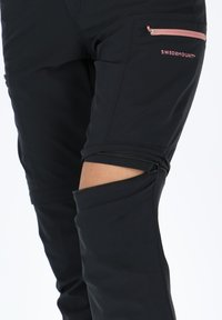Black hiking pants with a zippered alteration feature at the knees. Includes side pockets with pink zipper accents and a logo.