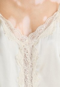 Primo piano di un neckline in satin con bordi in pizzo crema contro la pelle con macchie chiare.