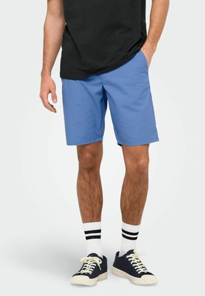 Blå shorts lavet af letvægtsstof, med en lige pasform, sidelommer og en glat overflade. Båret med sorte sneakers og stribede sokker.