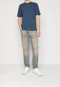 Námornícky modré bavlněné tričko s kulatým výstřihem a krátkými rukávy, v kombinaci s světle modrými džíny a bílé tenisky. Logo na hrudi.