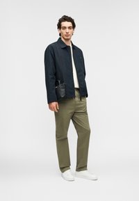 Ναυτικό σακάκι, λευκό πουκάμισο, παντελόνι ελιάς και λευκά αθλητικά παπούτσια. Μικρή μαύρη τσάντα χιαστί. Λείο ύφασμα, άνετη εφαρμογή, μίνιμαλ σχεδιασμός.