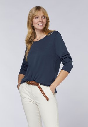 Navy blue long-sleeve top with a round neckline, paired with cream-colored pants and a braided brown belt; smooth fabric with a relaxed fit.
