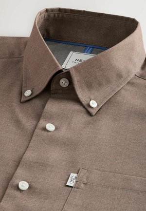 Braunes Hemd mit Knöpfen, das einen klassischen Kragen, weiße Knöpfe, eine schlichte Brusttasche und eine subtile Textur aufweist, mit einem Etikett in der Ecke.