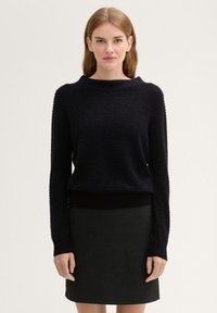 Schwarzer strukturierter Pullover mit weitem Ausschnitt und enganliegenden Bündchen, kombiniert mit einem schwarzen Rock. Glattes Material mit dezenten Mustern.