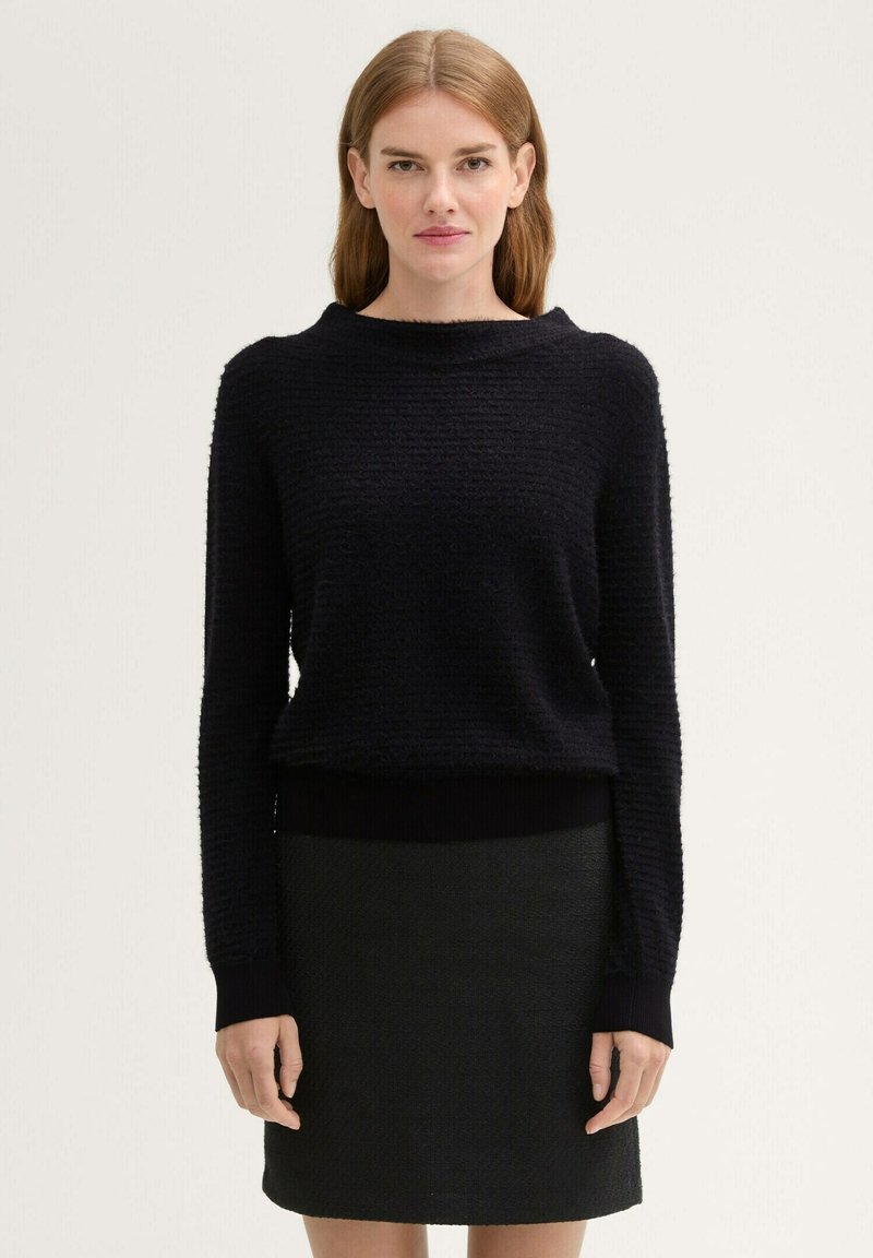 Schwarzer strukturierter Pullover mit weitem Ausschnitt und enganliegenden Bündchen, kombiniert mit einem schwarzen Rock. Glattes Material mit dezenten Mustern.