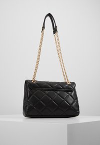 Borsa a tracolla nera trapuntata in pelle, con una tracolla in catena dorata e un design strutturato. La superficie ha una finitura lucida e testurizzata.