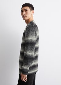 Grau und schwarz gestreifter Pullover mit weicher Textur, Rundhalsausschnitt und langen Ärmeln, getragen mit schwarzen Hosen, vor einem schlichten Hintergrund.