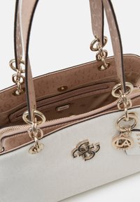 Hvid håndtaske med en tekstureret overflade, guldfarvet hardware og en beige foring. Har et logo og flere rum til organisering.