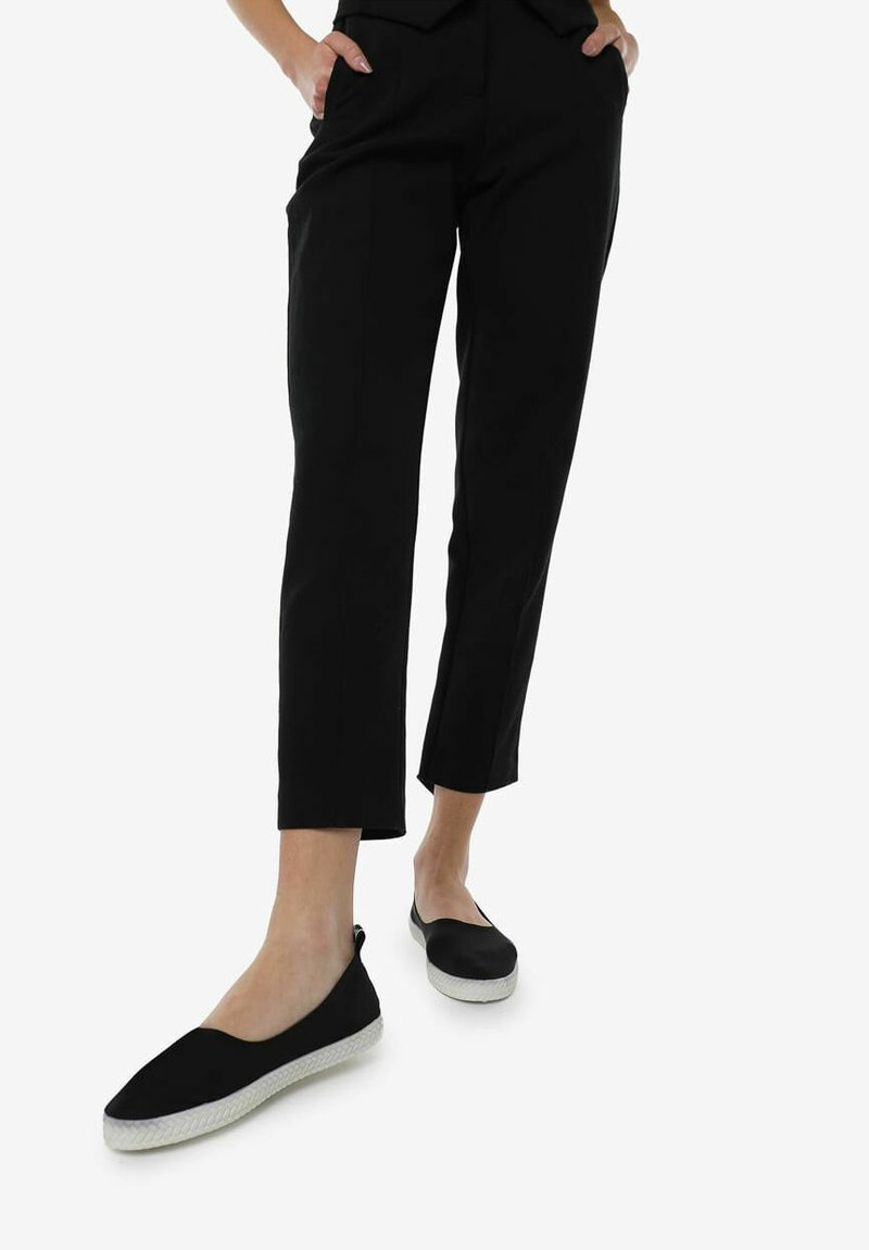 Sorte bukser med slim fit og ankellængde, parret med sorte slip-on sko med en hvid gummisål og vævet tekstur.