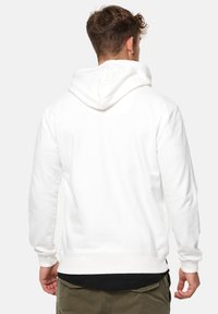 Weißer Hoodie mit weicher Textur, ausgestattet mit einer großen Kapuze, gerippten Bündchen und einem gerippten Saum. Das Design ist schlicht, ohne sichtbare Muster oder Hardware.