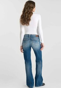 Jean évasé bleu avec un design décoloré, comportant deux poches arrière et une étiquette en cuir au niveau de la taille. Fabriqué en denim.