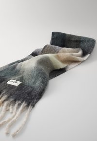 Écharpe en laine avec un dégradé de gris, sarcelle et beige, offrant une texture douce et des bords frangés. Étiquette de marque visible.