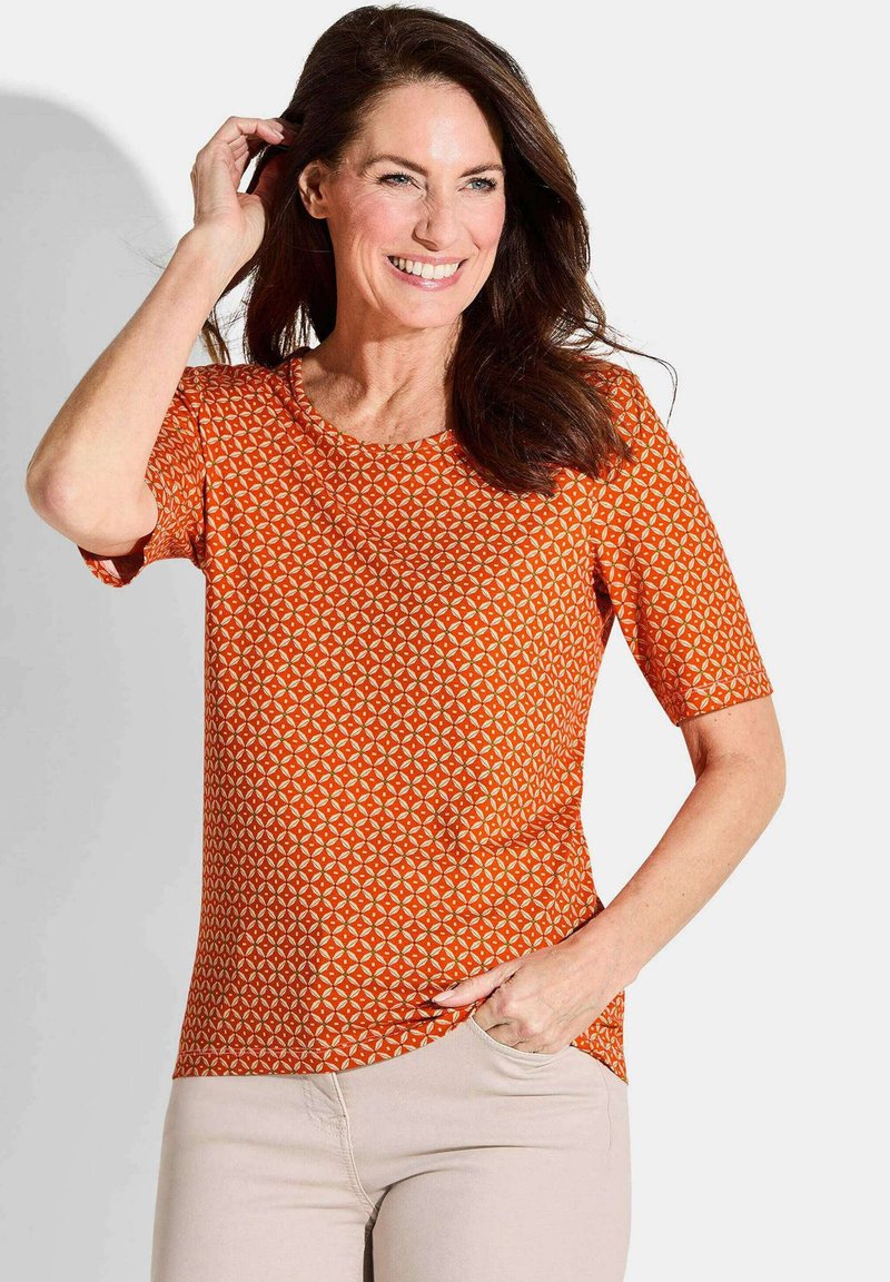 Korte mouw oranje top met geometrisch patroon, ronde halslijn en een licht gebogen zoom. Soepele stof, casual pasvorm, geen zichtbare sluitingen.