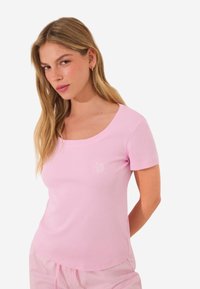 T-shirt rose à manches courtes en tissu doux, dotée d'un col rond et d'un petit logo sur la poitrine gauche. Texture lisse, coupe régulière.