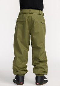 Grüne, weit geschnittene Hosen mit strukturierter Oberfläche, die mehrere Taschen und ein Sterne-Symbol auf der Rückseite haben. Kombiniert mit schwarzen Sneakers.