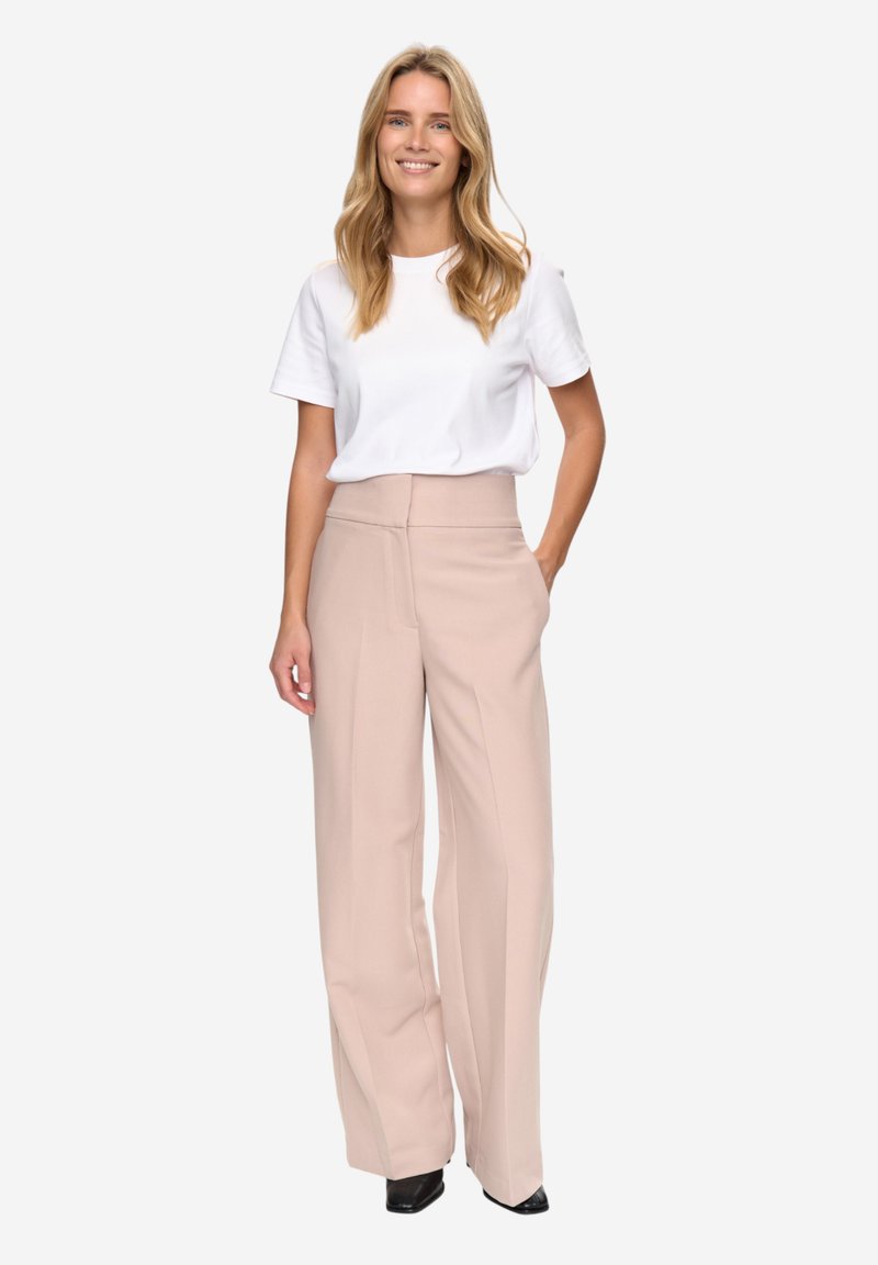 T-shirt blanc à manches courtes associé à un pantalon beige taille haute à jambes larges. Le pantalon possède des poches avant et une texture lisse.