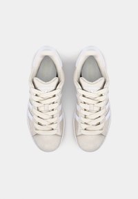 Beige sneakers med overdel av semsket skinn, hvit gummisåle og tre hvite striper. Har strukturert snøring og polstret krage.