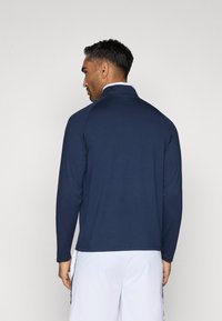 Camisa azul-marinho de manga longa com gola alta, feita de tecido suave. Apresenta um design sem emendas e um corte ligeiramente ajustado.