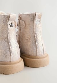 Stivali rosa oro con finitura texturizzata, fodera in pelliccia e suola chiara. Presentano dettagli a forma di stella argentata e chiusura con zip.