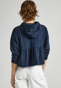 Sudadera con capucha de color azul marino con diseño peplum, que presenta mangas largas y puños acanalados. Tejido suave con un corte relajado.