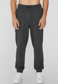 Graue Jogginghosen mit Kordelzug und elastischen Bündchen, aus weichem Stoff hergestellt. Sie haben eine schmale Passform und werden mit weißen Sneakern getragen. Keine Muster oder Verzierungen.